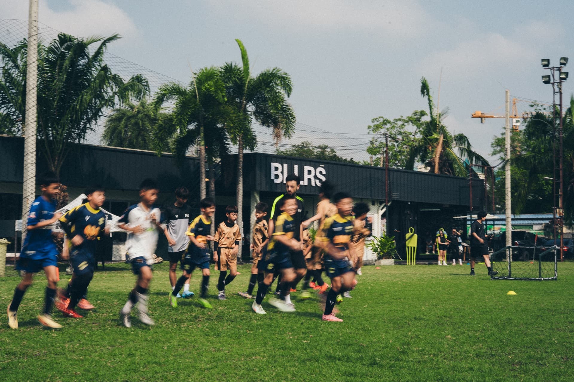 BALLERS Bangkok — players running on the pitch with BLLRS facility in the background