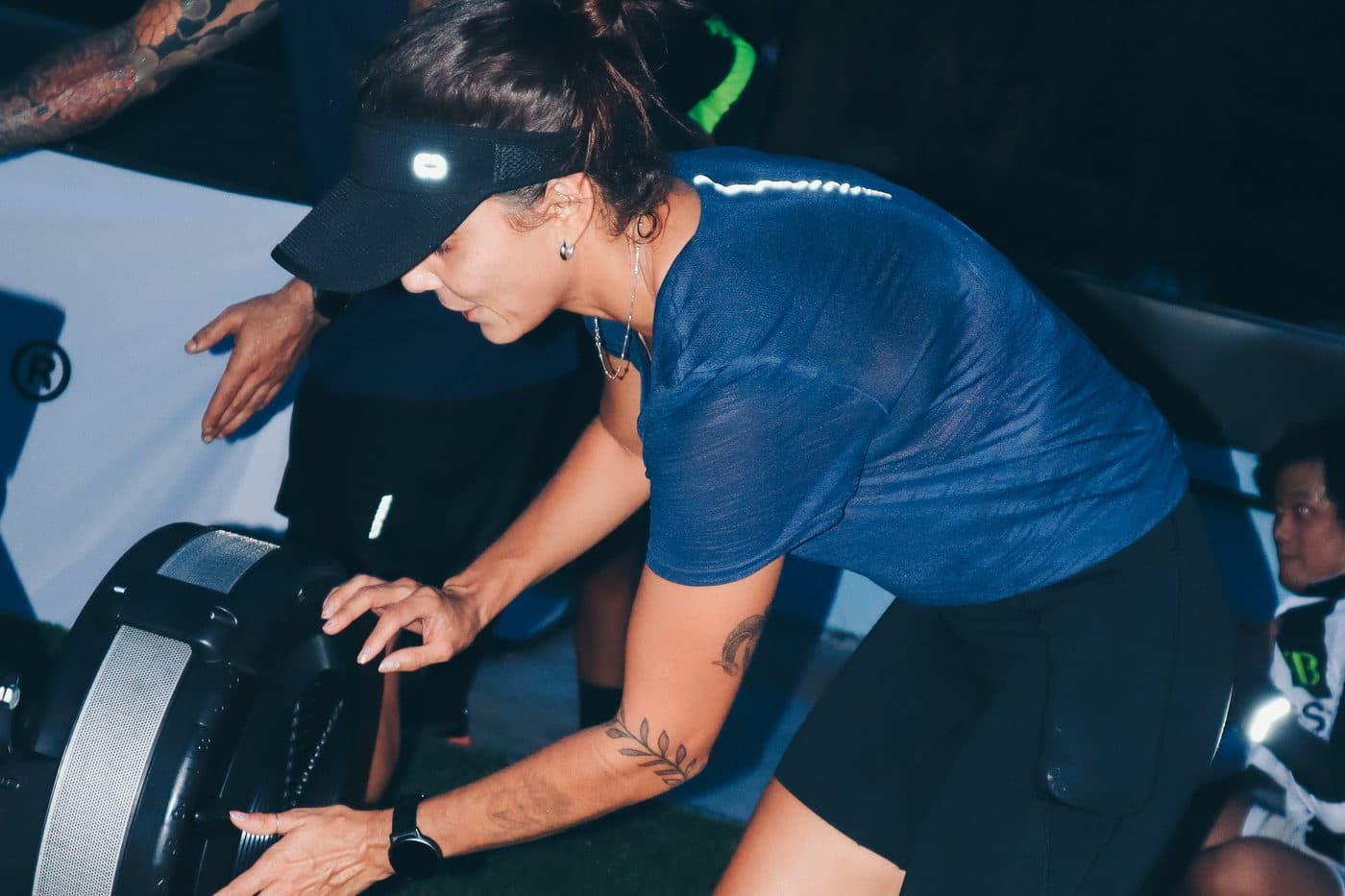 A participant rowing under the lights, with a coach watching beside her