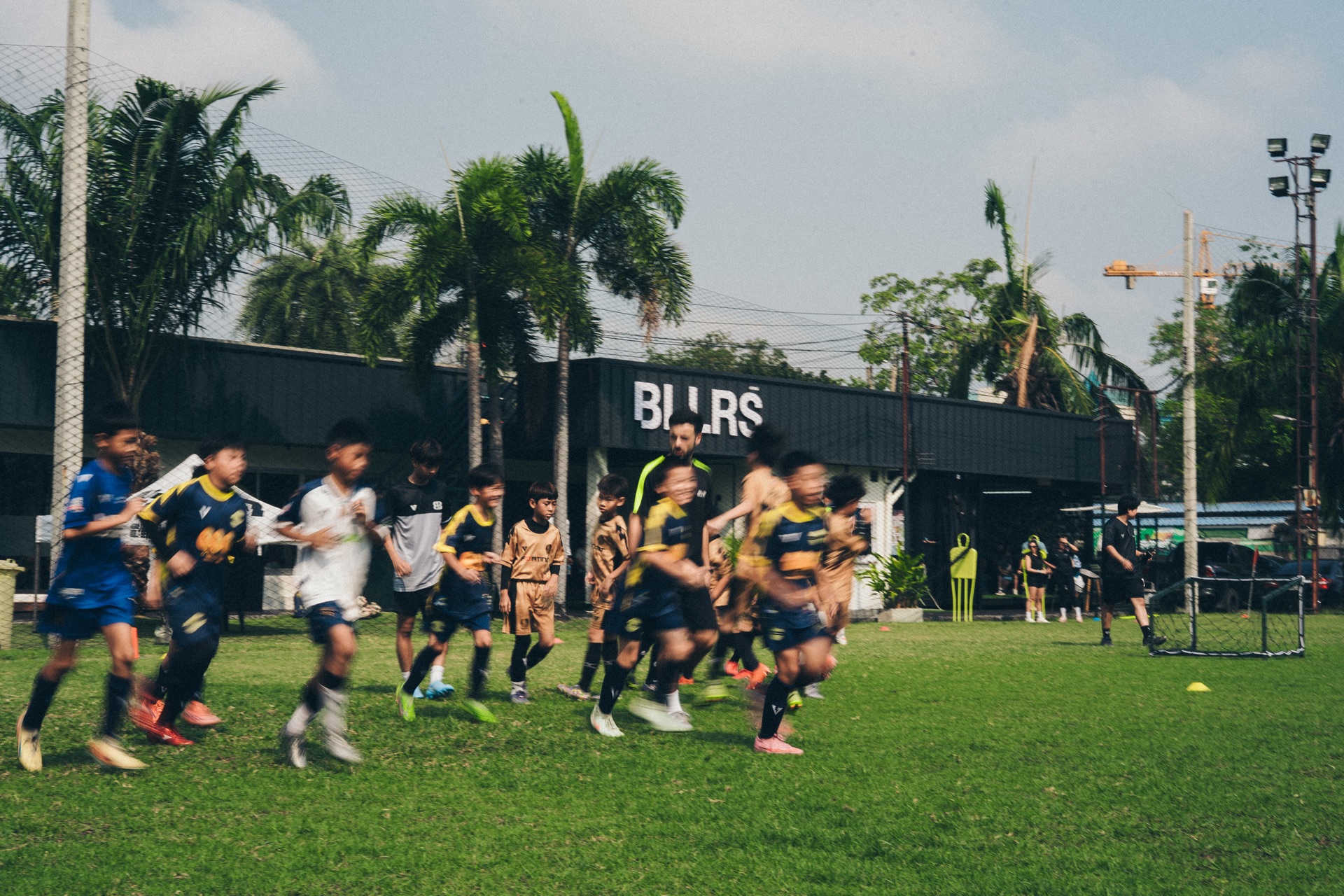 BALLERS Bangkok — players running on the pitch with BLLRS facility in the background